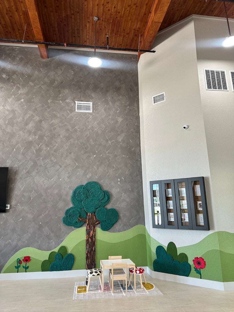 Wide view of the Pinnacle Montessori lobby with a wood ceiling, dimensional yarn tree, green hill mural, and children's table.