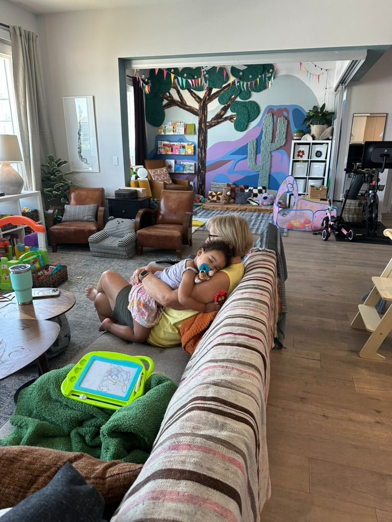 Family relaxing in a living room that opens onto a playroom with handmade yarn tree and cactus wall art.