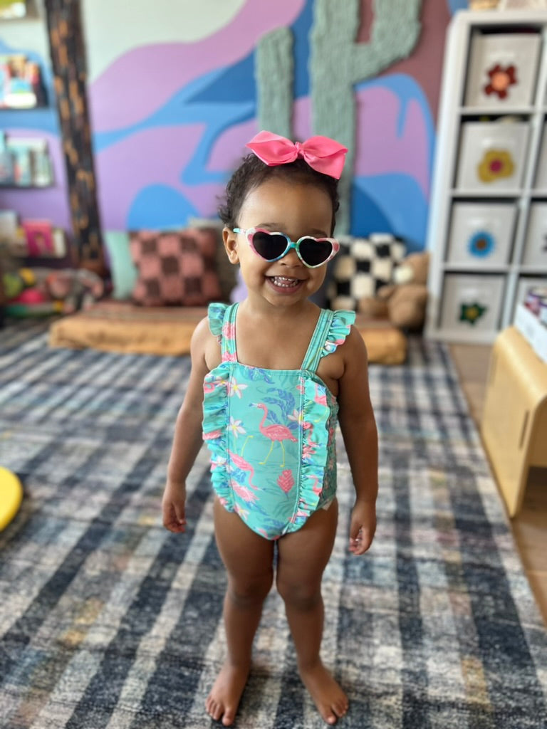 A child playing in sunglasses in front of the handmade yarn cactus and colorful mountain mural in a family playroom.