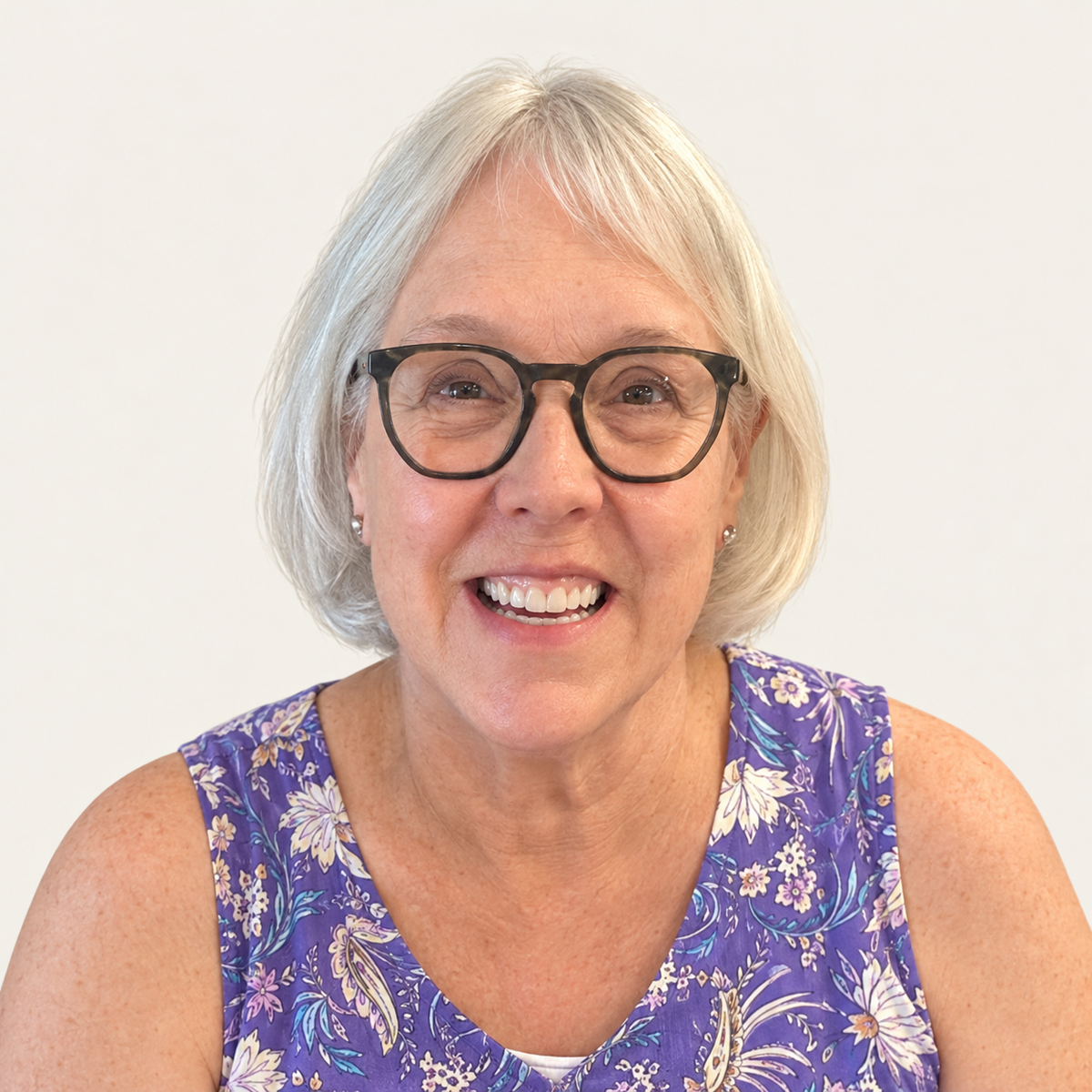 Nonnie smiling in glasses and a purple floral top against a warm beige background.